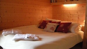Una stanza con rivestimento in legno, un letto, cuscini e un comodino con una lampada.
