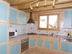 A kitchen with light blue cabinets, a white microwave, a stove, a sink, and a window with a view of the outside. - Spacious chalet for 10 people with WiFi and fireplace (Les Gets)