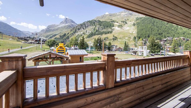Une terrasse en bois offrant une vue sur un paysage montagneux, avec notamment un télésiège et des bâtiments.