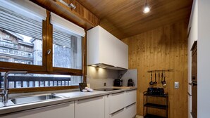 Une cuisine moderne avec des meubles blancs, un plafond en bois et une vue sur le paysage urbain, visible à travers une grande fenêtre.