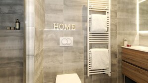 A modern bathroom with a grey tiled wall, a white towel rack, a toilet, and a wooden vanity. - New Ski-In/Ski-Out, 3 Bedrooms with WiFi and Parking (Courchevel 1650)