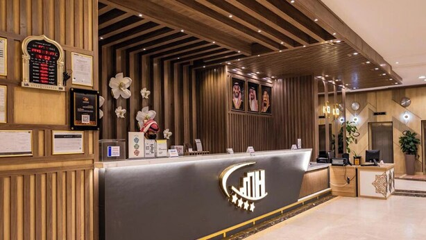 A hotel reception desk with a modern design, featuring a logo, a digital display, and a floral arrangement.