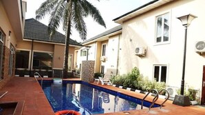 A swimming pool with a tiled deck, a palm tree, and a building with air conditioning units. - Cromwell Courtyard hotel (Lagos)