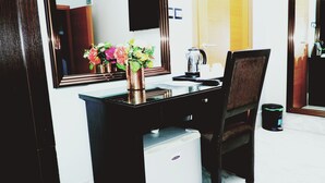 A hotel room with a wooden desk, a mirror, a vase with flowers, a kettle, and a trash bin. - Cromwell Courtyard hotel (Lagos)