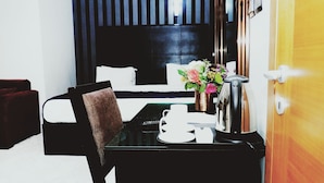 A hotel room with a bed, a desk with a chair, a coffee maker, a vase with flowers, and a door. - Cromwell Courtyard hotel (Lagos)