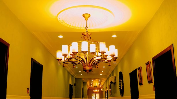 A hotel hallway with a large chandelier, framed artwork on the walls, and doors on either side. - Cromwell Courtyard hotel (Lagos)