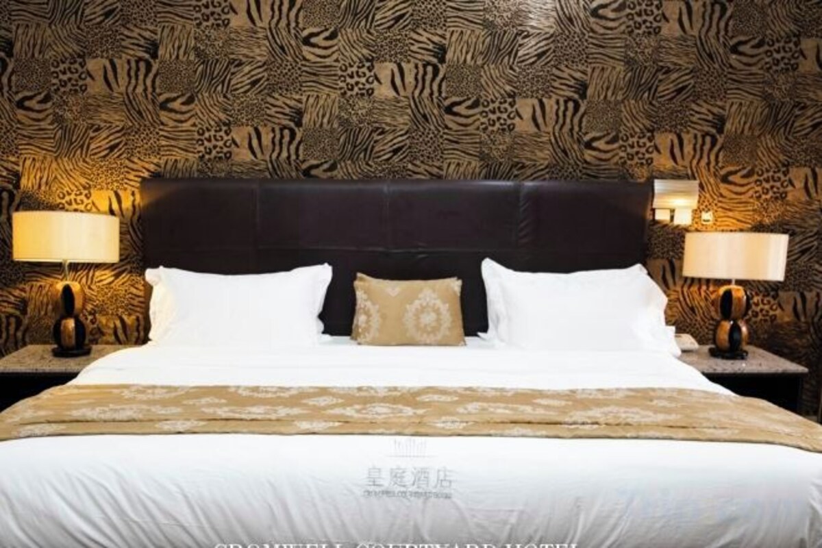 A hotel room with a patterned wallpaper, a large bed with white linens, two bedside tables with lamps, and a headboard.