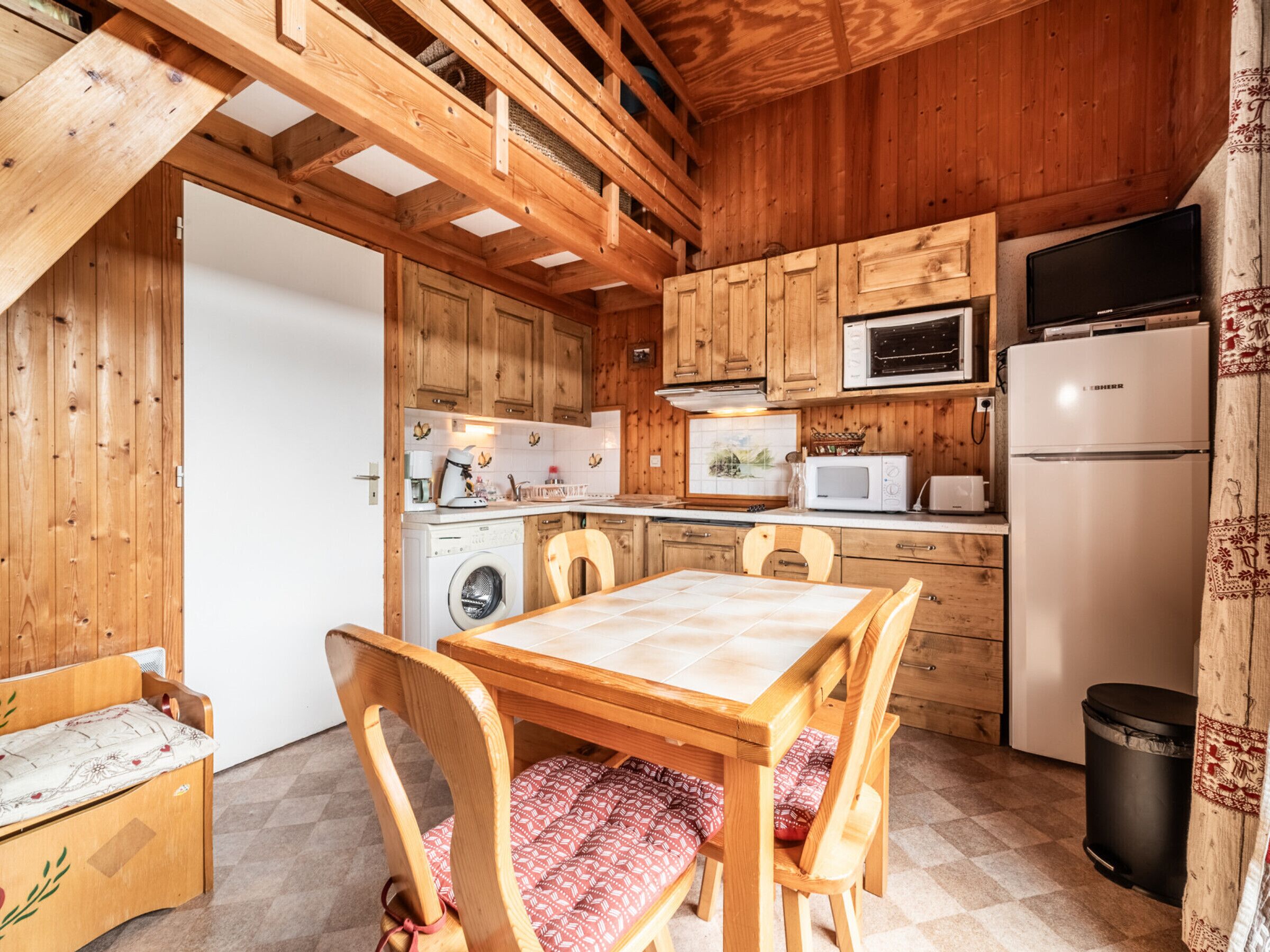 Eine kleine Küche mit Holzausstattung, einer Mikrowelle, einem Kühlschrank und einer Waschmaschine.