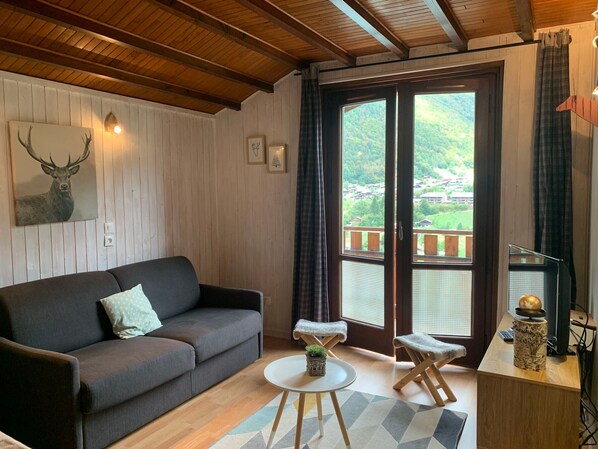 Relax in this inviting living space with a sofa, round table, and potted plant, offering a view of the lush landscape from the balcony.