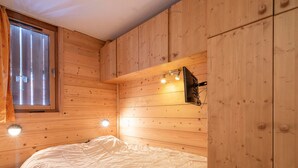 Ein Zimmer in einer Holzhütte mit einem Bett, einem Fenster und einem an der Wand befestigten Fernseher.