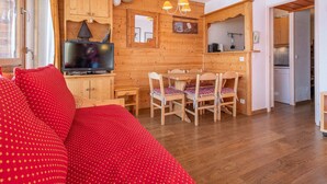 Ein gemütliches Zimmer mit Holzvertäfelung, einem Fernseher, einem Esstisch mit Stühlen und einem roten Sofa.
