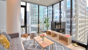Ein modernes Wohnzimmer mit einer Couch, einem Couchtisch, einem Fernseher und großen Fenstern mit Blick auf die Stadt.