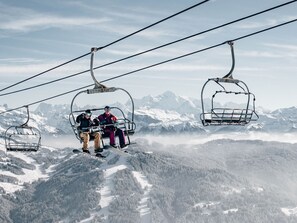 A ski lift with passengers, surrounded by snow-covered mountains and forested slopes. - Cozy apartment: 1 bed, parking, WiFi, pets allowed (Les Gets)