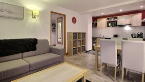 Un espacio habitable compacto con sofá, mesa de comedor y sillas, kitchenette con armarios y electrodomésticos, y un espejo en la pared.