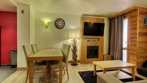 Una sala de estar con una mesa de comedor de madera, un sofá, un televisor montado en una pared de madera y una chimenea.