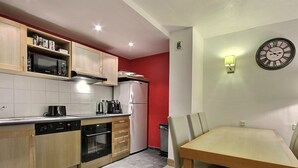 Una cocina moderna con armarios de madera, un microondas, una estufa y un refrigerador. Hay una mesa de comedor con sillas y un reloj de pared.