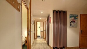 Un pasillo con suelo de madera, una cama a la izquierda, una puerta de baño y un cartel en la pared.