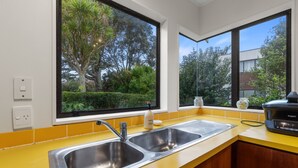A kitchen with two sinks, yellow countertops, and large windows offering views of greenery. - Central Comforts - Mount Eden Holiday Home (Auckland)