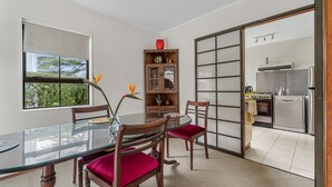 A dining area with a glass table, wooden chairs with red cushions, a wooden cabinet with glass doors, and a view of a kitchen through a sliding door. - Central Comforts - Mount Eden Holiday Home (Auckland)