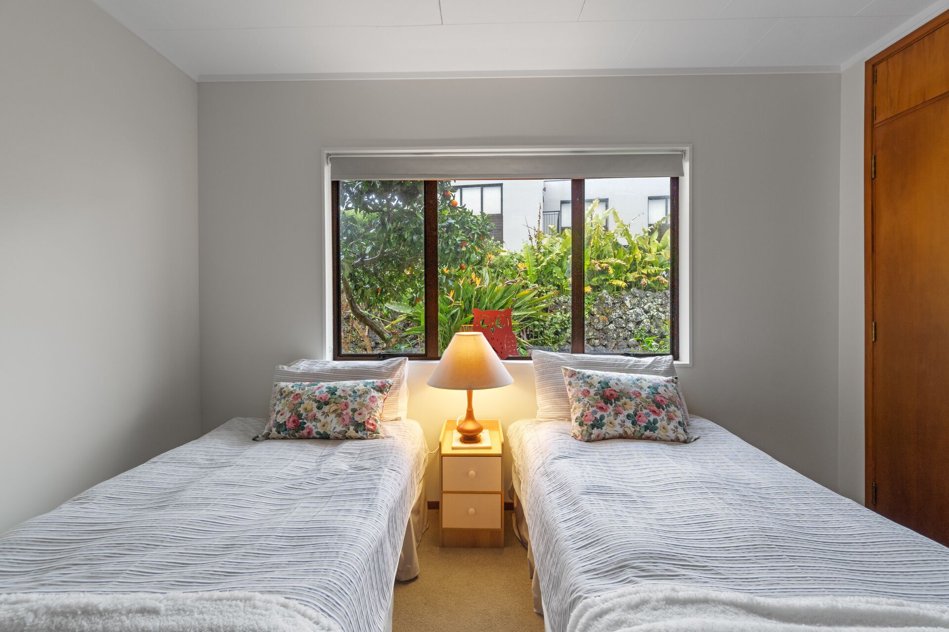 Une chambre avec deux lits, une table de chevet, une lampe et une fenêtre donnant sur un paysage verdoyant.