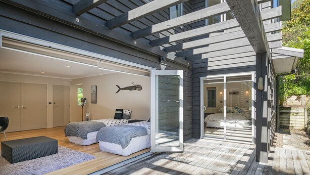 A modern bedroom with a large bed, a small seating area, and a sliding glass door leading to a balcony.