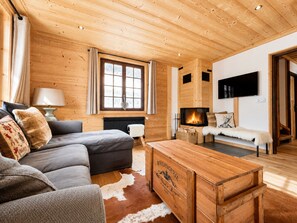 A cozy wooden interior with a sofa, a fireplace, and a television mounted on the wall.