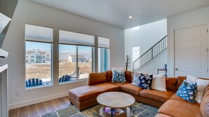 Una sala moderna con un sofá modular, una mesa de centro y grandes ventanales con vistas a un paisaje montañoso.