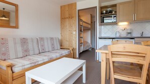 A compact living space with a sofa, a white table, a wooden chair, a bunk bed, and a kitchenette. - Charming studio for 4 in Avoriaz with balcony (Avoriaz)