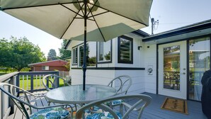 Eine Terrasse mit Tisch und Stühlen mit Glastischplatte, einem großen Sonnenschirm und einer Tür zu einem Innenbereich.