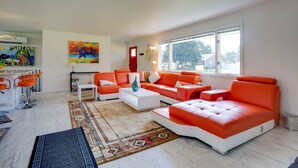 Ein modernes Wohnzimmer mit einer weißen und orangefarbenen Sofagarnitur, einem Couchtisch und einem farbenfrohen Teppich.