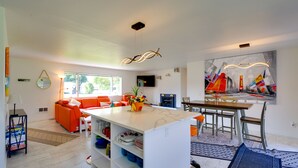 Eine moderne Küche mit einer zentralen Kochinsel, leuchtend orangefarbenen Sitzgelegenheiten und einem Essbereich mit Blick ins Freie.