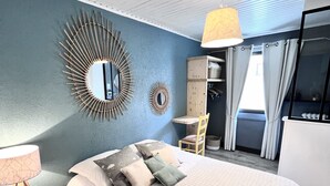 A bedroom with a bed, a wooden nightstand, a mirror, a hanging lamp, a wardrobe, a chair, and a window with curtains.