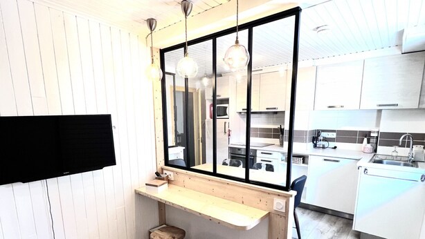 A compact kitchen with a wooden bar counter, stools, and a large window.