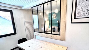 A room with a wooden table, black chairs, a window with blinds, and a wall-mounted light fixture.