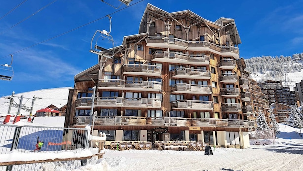Un edificio de madera de varios pisos con balcones, cables de telesilla y un paisaje nevado.