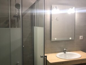 Ett badrum med en dusch som är avskärmad med glasväggar, ett handfat med en spegel ovanför och en bänkskiva i trä.
