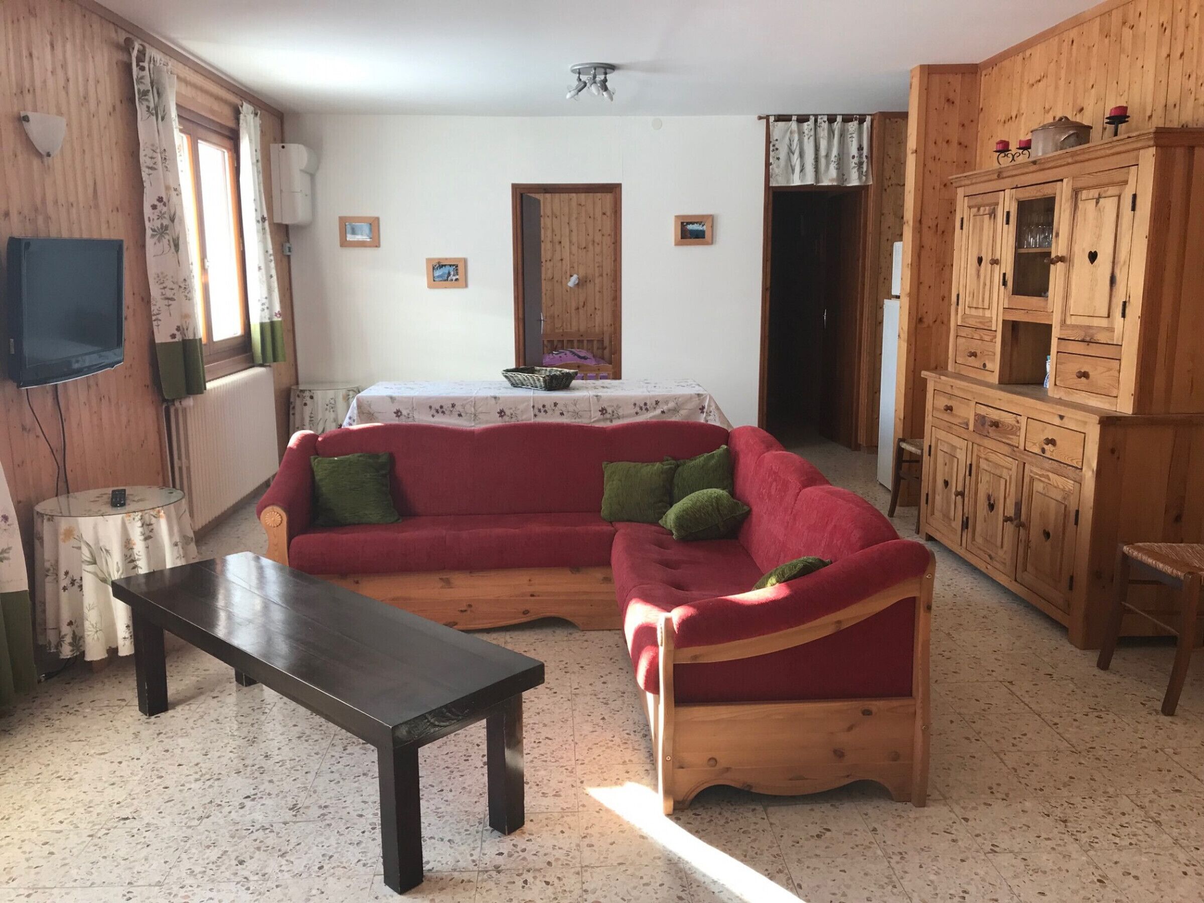 Un salon avec un canapé rouge, un meuble en bois, une télévision et une petite table ronde.