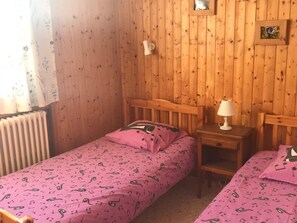 Ett mysigt rum med träväggar, en säng med ett rosa överkast, ett sängbord med en lampa och ett element.