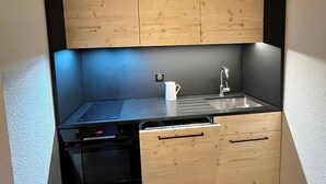 Eine kleine Küche mit Holzschränken, einer schwarzen Arbeitsplatte, einem Spülbecken und einem Geschirrspüler.