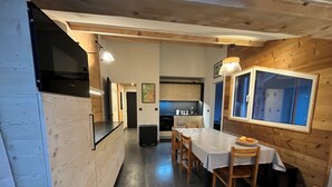 Ein Essbereich mit Tisch und Stühlen, im Hintergrund eine Küche und ein Fenster mit Jalousien.