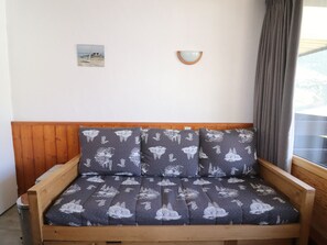 A wooden sofa with a dark patterned cushion, a small wall-mounted light fixture, and a picture on the wall.
