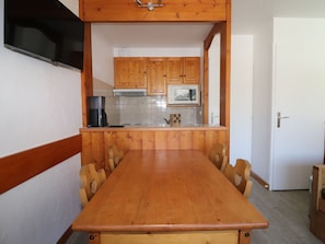 A wooden dining table with chairs, a coffee maker, and a microwave in a kitchen with wooden cabinets and a white tiled backsplash.