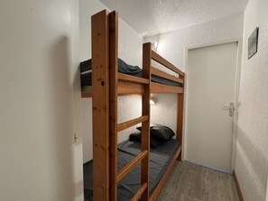 A bunk bed with a wooden frame and a mattress, a door, and a wall-mounted light fixture.