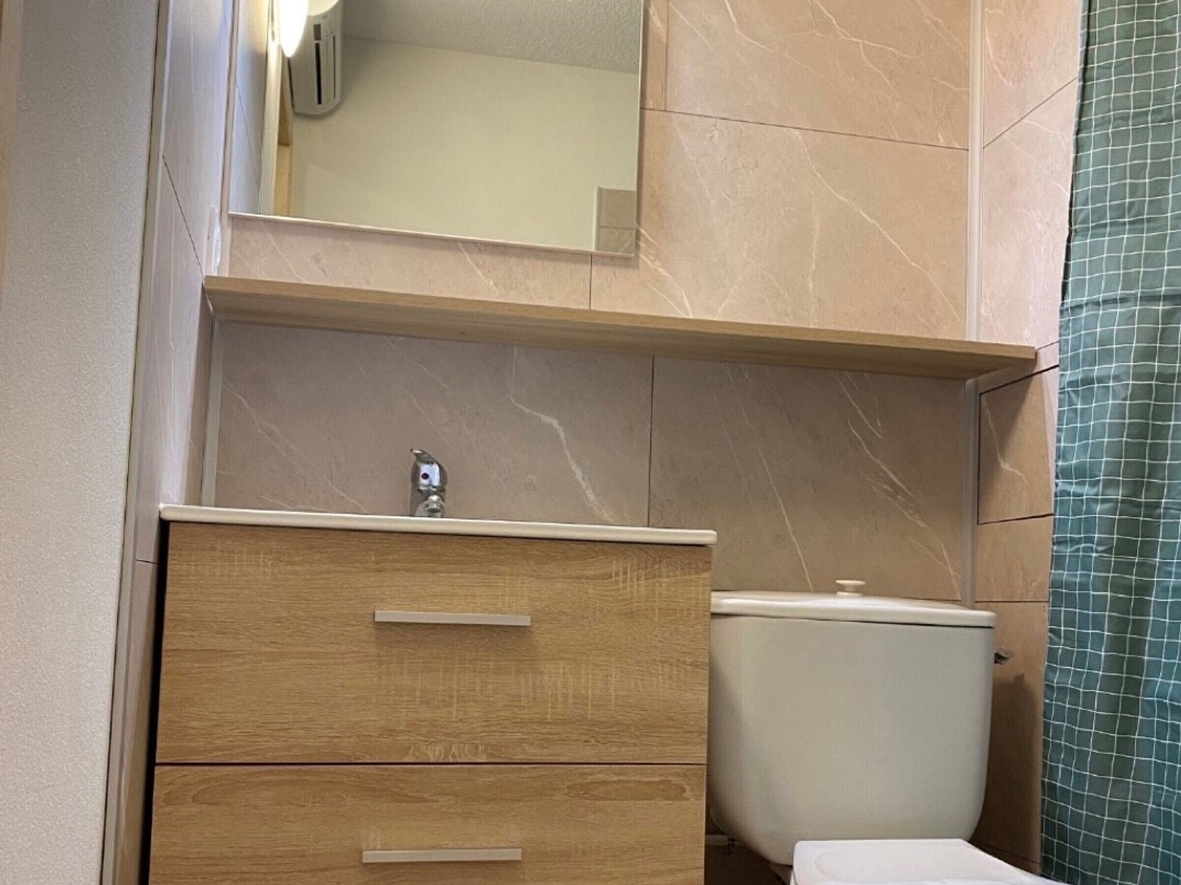A bathroom with a wooden vanity, a toilet, and a mirror above the vanity.