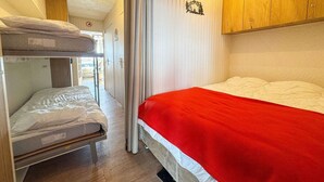Une petite pièce avec des lits superposés et un lit simple, des panneaux de bois et un rideau servant de séparation.
