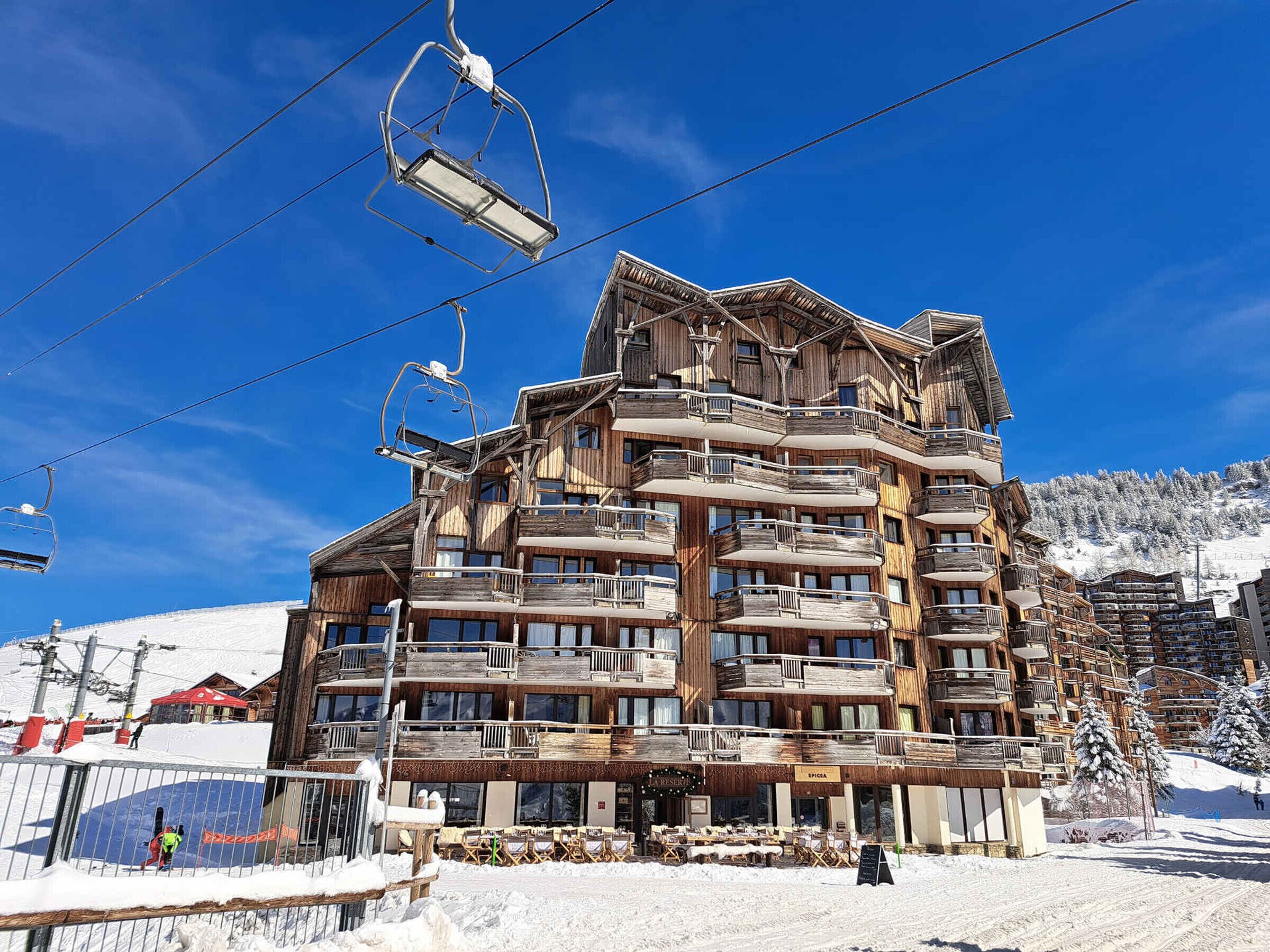 A multi-story wooden building with balconies, ski lift cables, and a snowy landscape.