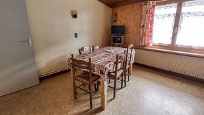 Un comedor con una mesa y sillas de madera, un televisor y un ventanal con cortinas.