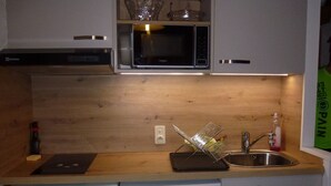 Ett kompakt kök med mikrovågsugn, diskmaskin och en diskho med ett diskställ.