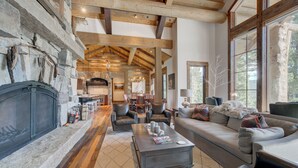A spacious living area with a stone fireplace, leather furniture, and large windows offering natural light. - Spanish Peaks Mountain Home - Big sky (Big Sky)