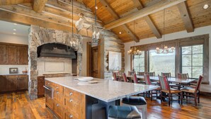 A spacious kitchen with a large island, wooden beams, stone accents, and a stone fireplace. - Spanish Peaks Mountain Home - Big sky (Big Sky)